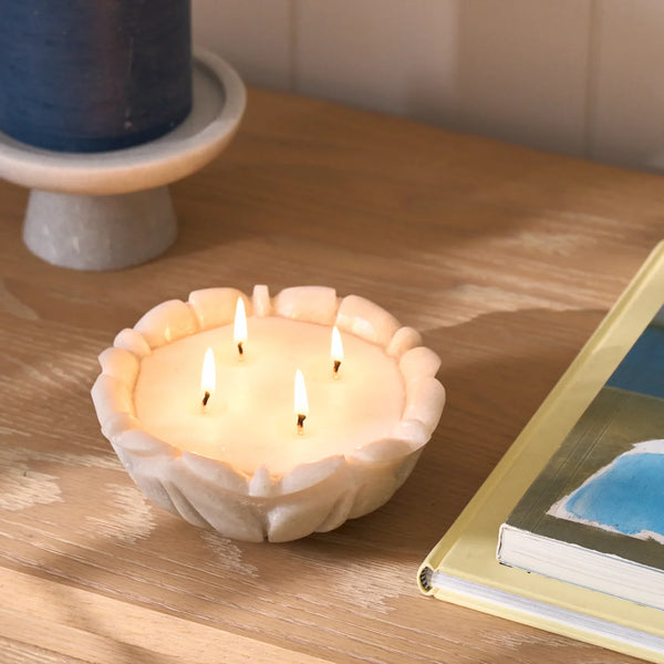 Malpas marble leaf design candle, lit on a wooden sideboard styled with books and pillar candle on stand