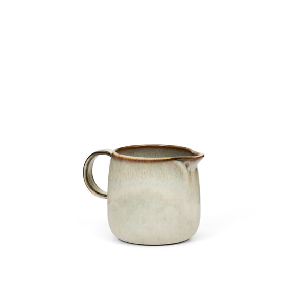 Cream ceramic milk jug with brown glazed rim on a white background