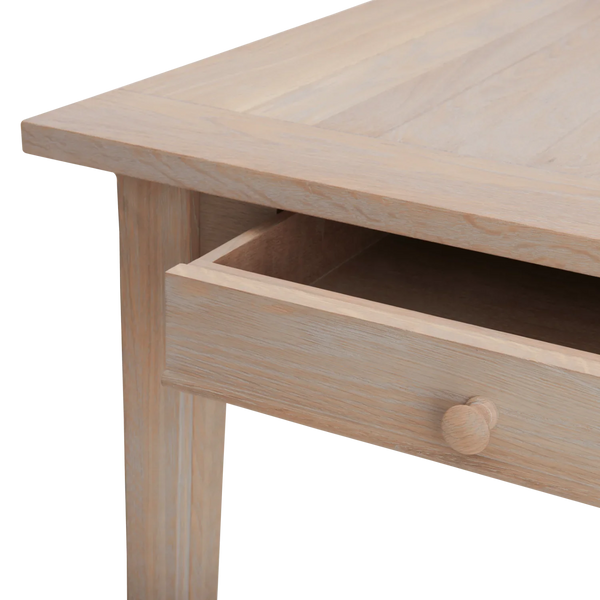 Close-up of a light natural wood table with an open drawer showing a round wooden knob, on a plain white background.