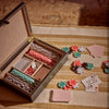 An open wooden card and chip box filled with poker chips, shown on a striped fabric surface with scattered playing cards and chip stacks nearby.