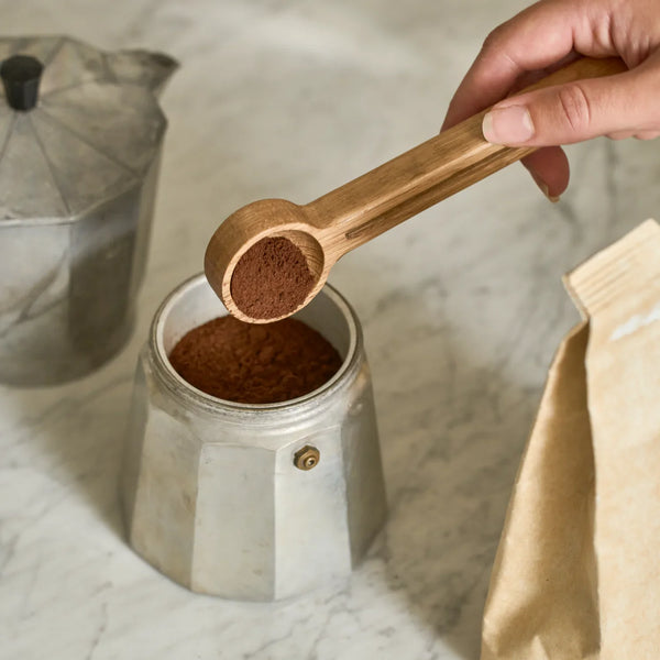 Orford wooden coffee scoop with roasted coffee bag on marble counter next to coffee pot