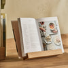 Orford white oak wooden cookbook stand holding recipe book, displayed on wooden counter