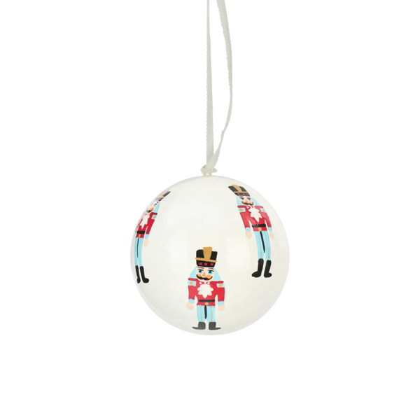 A white spherical Christmas ornament featuring a printed design of toy soldier figures in red, light blue, black, and gold uniforms, suspended by a white string against a plain white background.