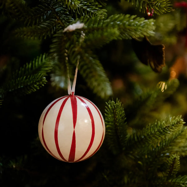 A round Christmas ornament with red and white vertical stripes hanging from a green Christmas tree branch.