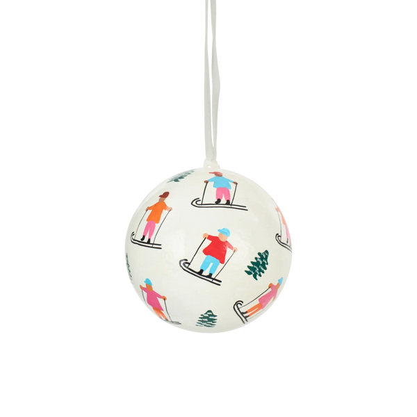A white spherical ornament with a hanging loop, decorated with a colorful pattern of skiers and small trees, shown against a plain white background.
