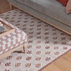 A woven area rug with a cream base and repeating brown and rust medallion motifs, styled in a living room under a gray sofa and a wooden ottoman.