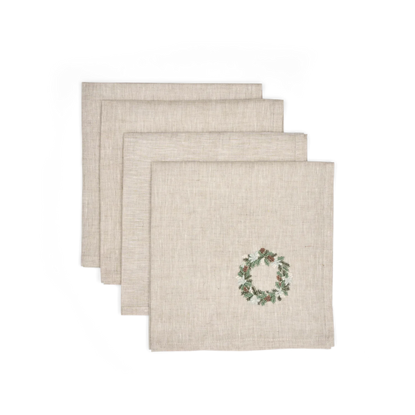 Three square beige linen napkins stacked in a fan arrangement, with a small embroidered green and red wreath on the front napkin, shown on a plain white background.