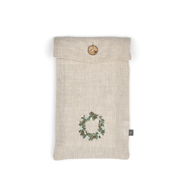 A light beige linen pouch with a green and red holly wreath embroidery on the front, featuring a wooden toggle closure at the top and a small black brand tag on the side.