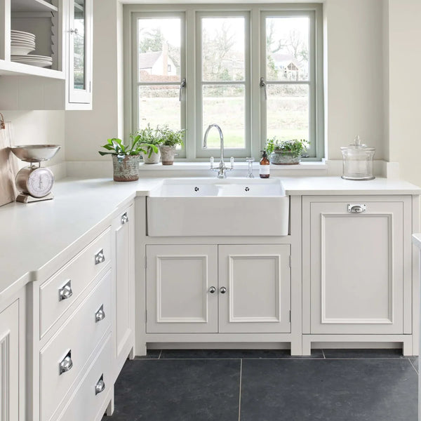 A contemporary country kitchen painted in shell white. With ceramic butler sink, chrome hardware. Stone tile flooring