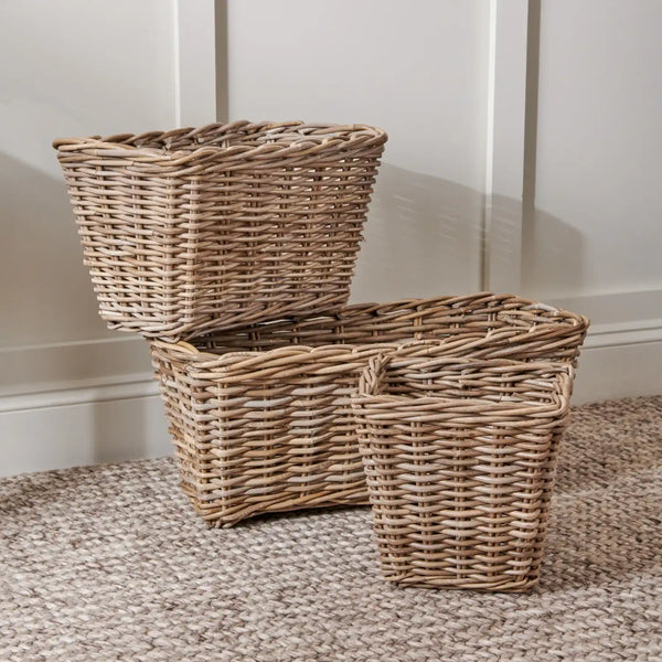 Three natural woven wicker storage baskets in different sizes, arranged on a textured beige rug against a white paneled wall.