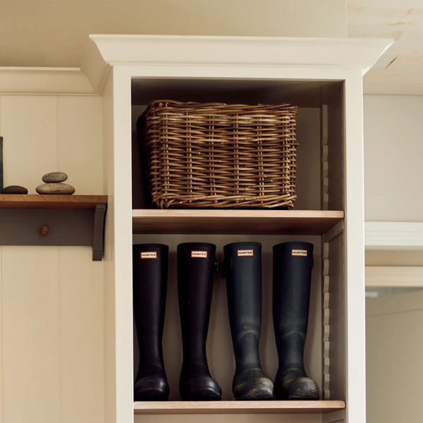 A woven wicker basket displayed on a wooden shelf next to a pair of black Hunter rain boots in a white built-in cabinet.