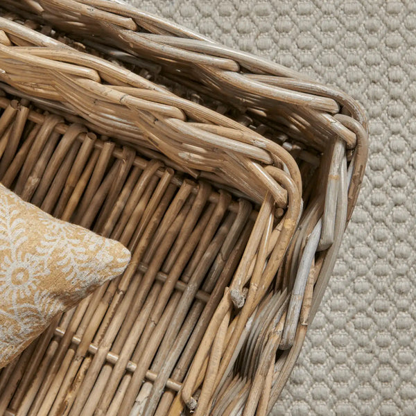Close-up of a woven natural rattan basket with a textured cream pillow on a woven rug.