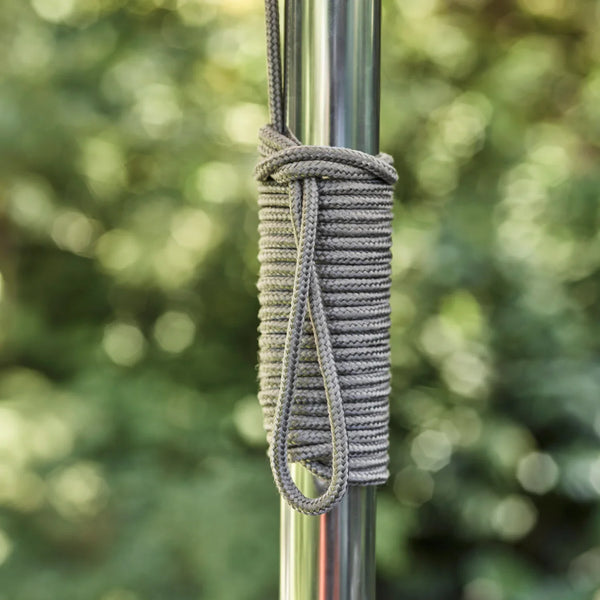 A close-up of a gray braided rope wrapped around a silver metal pole, with a looped end hanging down, set against a blurred green outdoor background.