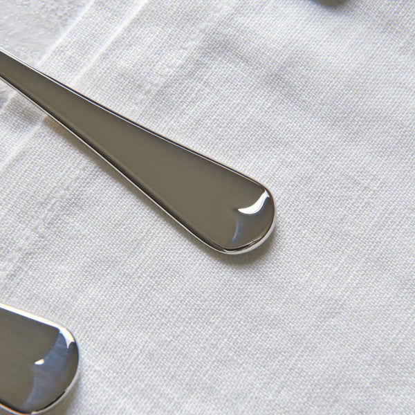 Close-up of polished silver metal spoon or spatula handles resting on a textured off-white fabric surface.