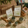 A styled picnic scene with a wicker picnic basket, two bags of Fire + Flow Cotswold coffee, a pack of biscuits, and a ceramic mug and espresso set on a woven tablecloth.