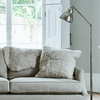 Sheepskin cushion on a light beige fabric sofa in a bright room, styled with  a tall silver floor lamp.