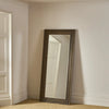 A tall, full-length floor mirror with a distressed dark brown wooden frame, leaning against a beige wall in a neutral room corner.