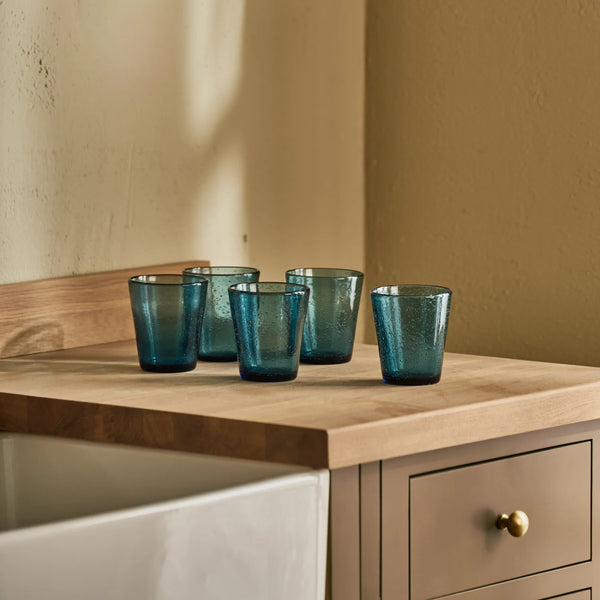 Six small blue textured glass tumbler s with a speckled finish, shown on a kitchen countertop with a neutral background.