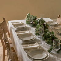 Dining table set with plates, glasses, and a festive greenery centerpiece.